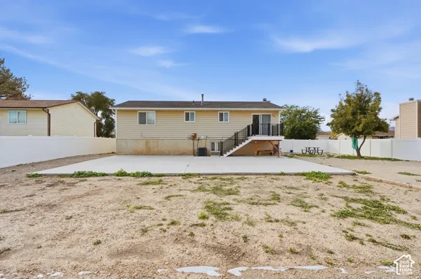 Backyard featuring a concrete patio, elevated deck with stairs, and white vinyl perimeter fencing