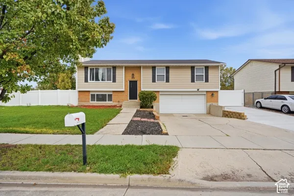 Split-level exterior featuring horizontal siding, brick masonry, an attached two-car garage, and a white privacy fence