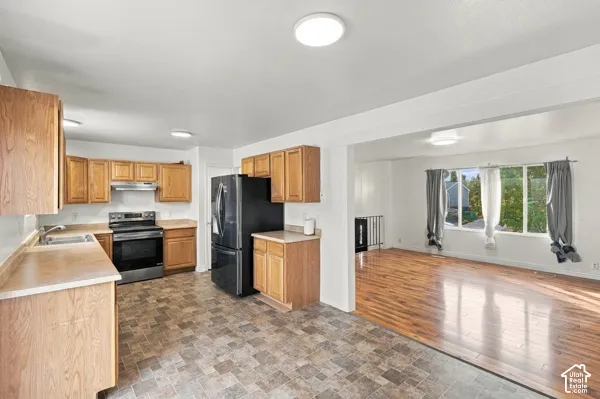 Kitchen featuring oak cabinetry, laminate countertops, a stainless steel range, and tile flooring, paired with a multi-pane window and wood-finish flooring