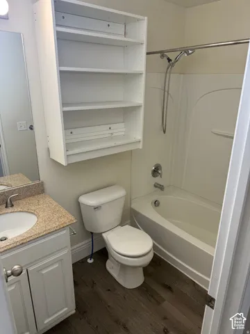 Bathroom featuring wood-finish flooring, a vanity with a stone-composite countertop, an integrated undermount sink, a built-in wall cabinet, and a bathtub-shower combination with a handheld fixture