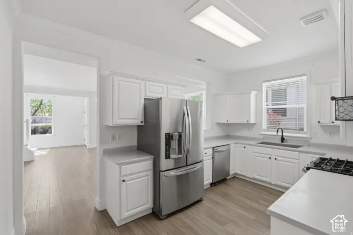 Kitchen featuring white cabinetry, wood-finish flooring, stainless steel refrigerator and dishwasher, solid-surface countertops, and a gas cooktop