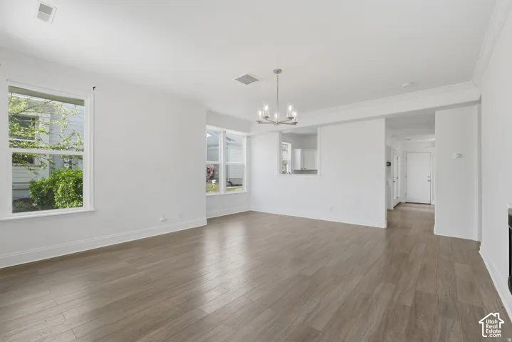 Open-concept interior featuring wood-finish flooring, crown molding, multi-pane windows, and a central chandelier