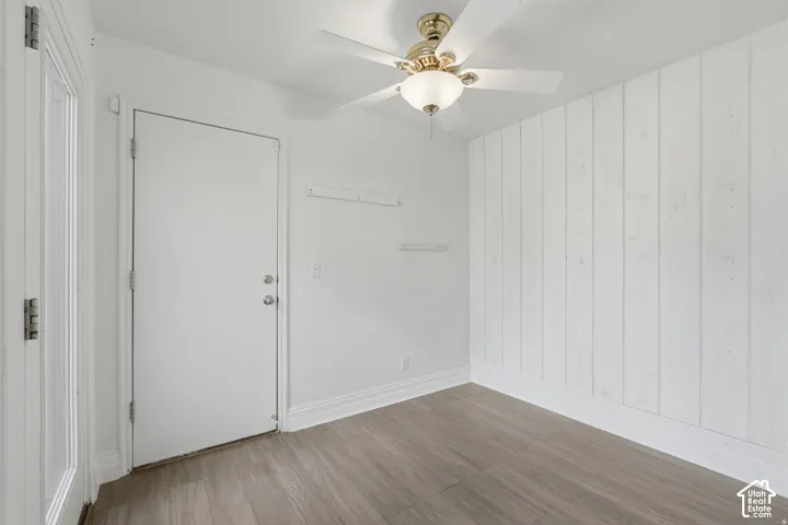 Interior room featuring vertical wood-plank wall paneling, wood-finish flooring, and a ceiling-mounted light fixture with a multi-blade fan