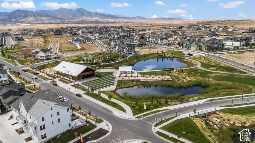 Aerial perspective of a community featuring natural ponds, terraced stone seating, a central pavilion structure, paved pedestrian pathways, and a mountain range backdrop