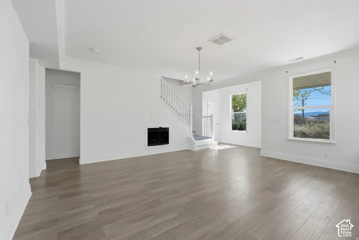 Living area featuring wood-finish flooring, a fireplace with a mantel, a multi-light chandelier, a white staircase with a wooden railing, and windows with white casings