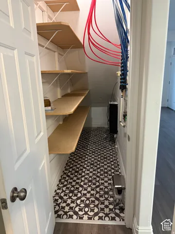 Storage space featuring tiered shelving, decorative patterned tile flooring, and exposed PEX plumbing manifold
