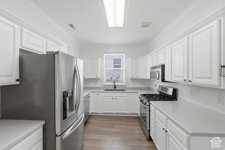 Kitchen featuring white shaker-style cabinetry, solid-surface countertops, stainless steel appliances, and wood-finish flooring