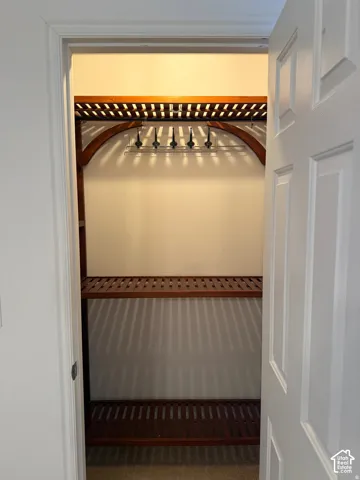 Storage area featuring custom wood-slatted shelving, arched support detailing, and a multi-hook hanging rack