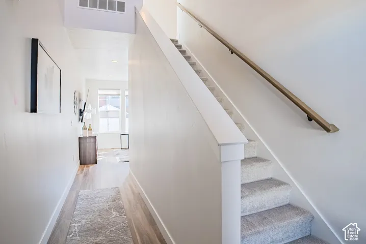 Entryway featuring wood-finish flooring, a carpeted staircase, and a wall-mounted handrail