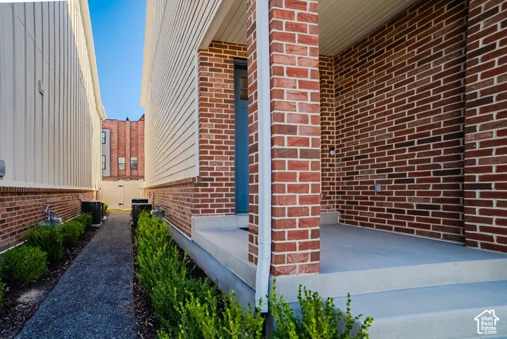 Exterior entrance featuring red brick masonry, horizontal lap siding, a concrete porch, and a dedicated walkway with low-profile shrubbery