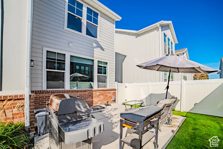 Rear exterior featuring horizontal lap siding, a lower-level brick veneer, a concrete patio, and a white privacy fence