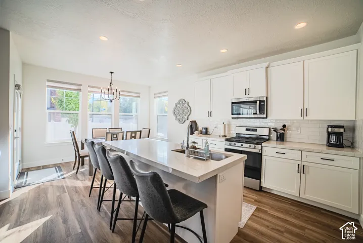 Kitchen featuring white cabinetry, stone-finish countertops, subway tile backsplash, stainless steel appliances, and wood-finish flooring
