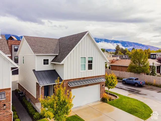 Exterior featuring vertical board-and-batten siding, brick masonry lower facade, standing-seam metal awning, asphalt shingle roof, and a concrete driveway