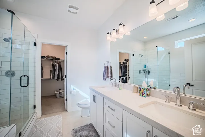 Dual-sink vanity with light-toned countertop, glass-enclosed shower featuring white tile surround, and extensive full-width wall mirror with multi-bulb overhead lighting