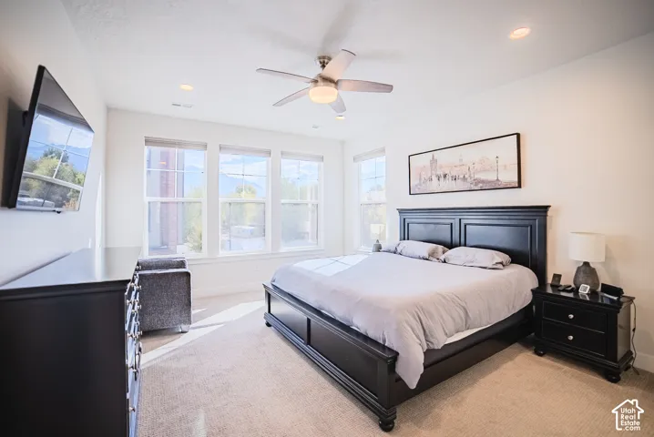 Neutral-toned wall-to-wall carpeting, multiple windows providing natural illumination, ceiling fan with central lighting, and recessed ceiling lighting