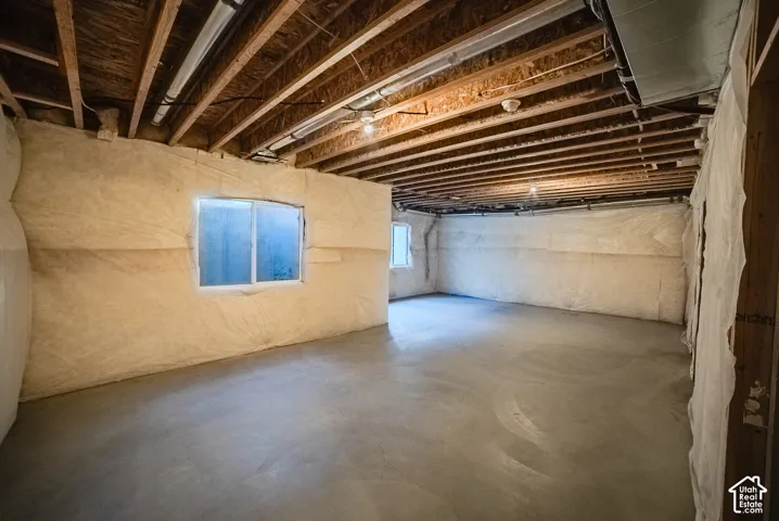 Unfinished interior space featuring exposed wood joist ceilings, concrete flooring, and insulated foundation walls with sliding windows