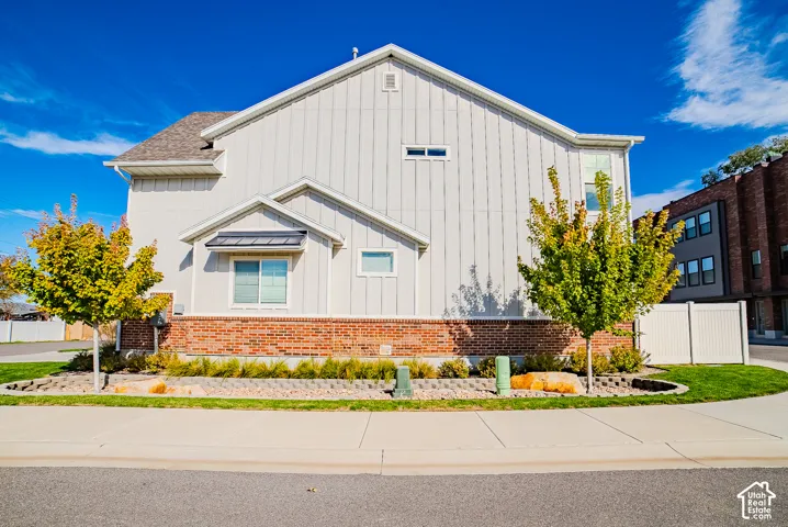 Exterior featuring vertical panel siding, brick veneer foundation, asphalt shingle roof, and landscaped garden bed with decorative stone borders
