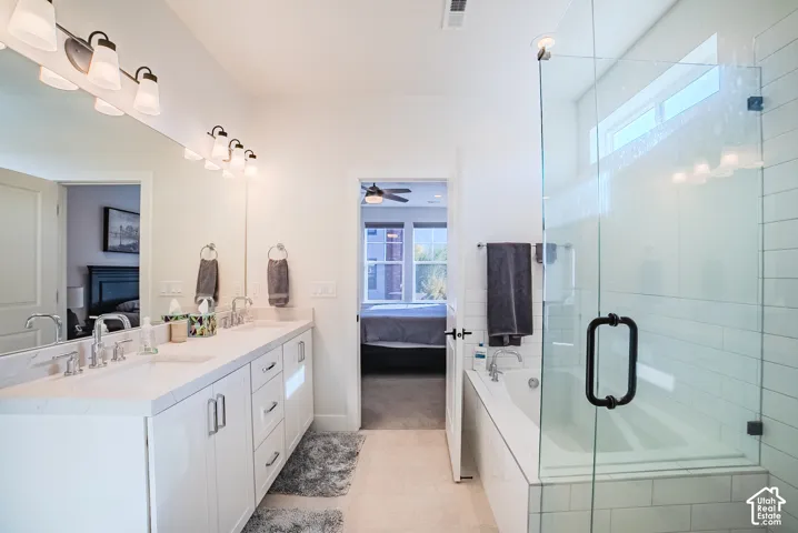Dual-sink vanity with white cabinetry and light-toned countertop, glass-enclosed shower, soaking tub with tile surround, and expansive wall-to-wall mirror