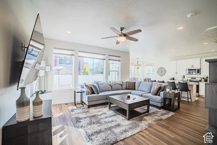 Open-concept living space featuring wood-finish flooring, recessed lighting, a brushed-nickel ceiling fan, large windows, and white cabinetry