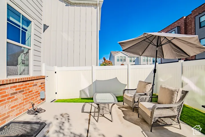 Private patio featuring concrete surfacing, brick masonry detailing, and enclosed by white vinyl fencing with a grass lawn