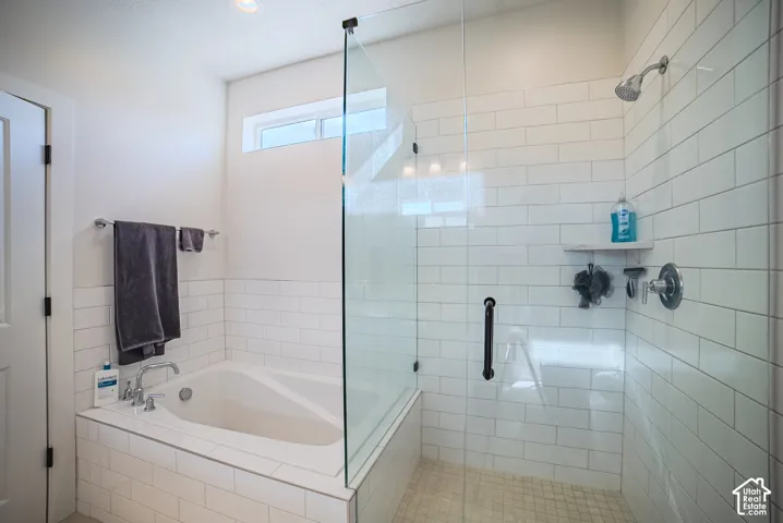 Bathroom featuring a white subway tile surround, deep soaking tub, glass-enclosed shower, polished chrome fixtures, and a transom window