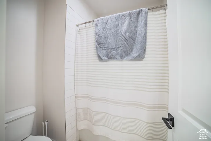 Full bathroom featuring a white porcelain toilet and a tub-shower enclosure with subway-style wall tile and a matte black door handle