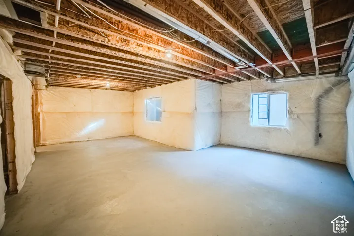 Unfinished lower level featuring concrete flooring, exposed wood-joist ceiling, and blanket-wrapped wall insulation with two inset windows