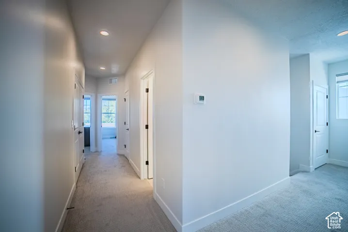 Hallway featuring neutral wall-to-wall carpeting, recessed ceiling lighting, multiple solid-core panel doors, and a digital thermostat