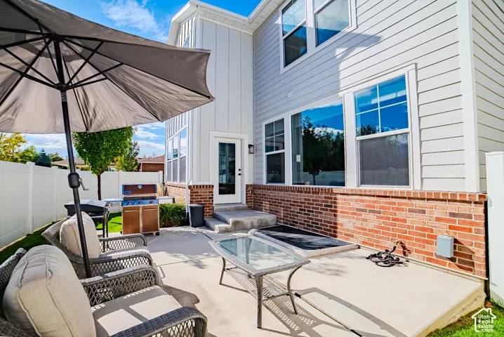 Rear exterior featuring a concrete patio, red brick masonry, light-toned horizontal siding, board-and-batten siding accents, and a white vinyl privacy fence