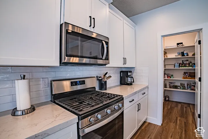 Kitchen featuring white cabinetry, stainless steel gas range, built-in microwave, stone-finish countertops, and subway tile backsplash, with an interior walk-in pantry