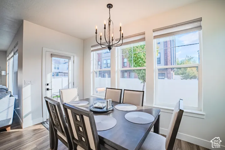 Dining area featuring wood-finish flooring, a tiered black metal chandelier, and large windows with roller shades