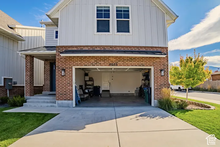 Exterior facade featuring vertical board-and-batten siding and a red brick lower level with a covered front porch, concrete driveway, and attached two-car garage