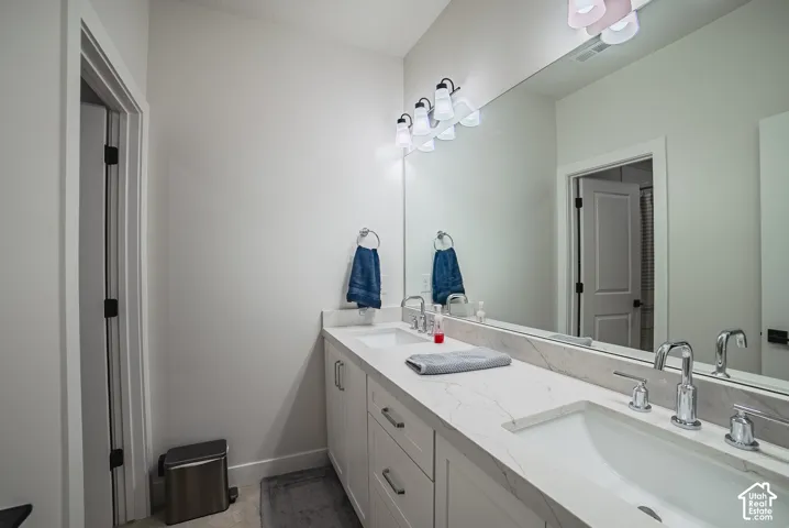 Dual-sink vanity featuring stone-finish countertops, white cabinetry with matte black hardware, integrated rectangular basins, chrome widespread faucets, and a full-width mirror
