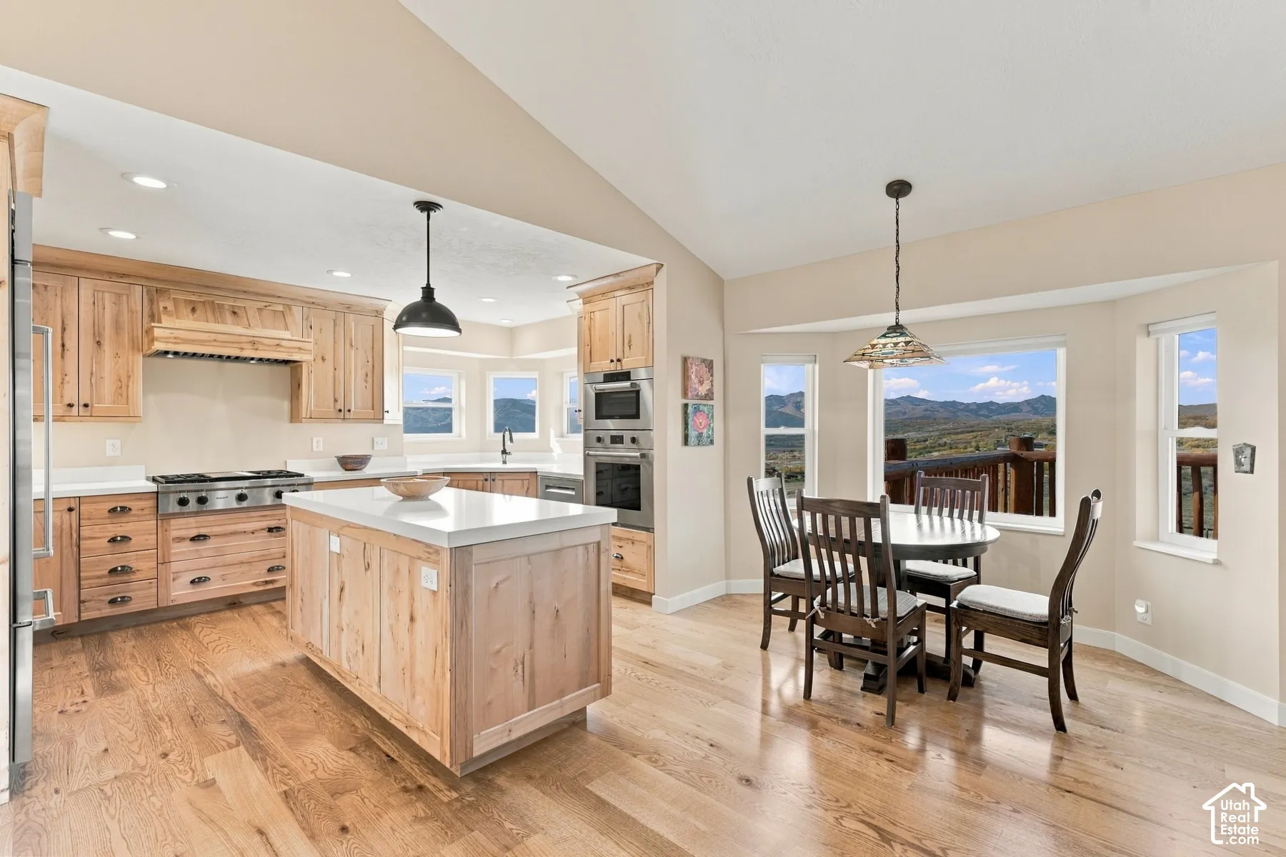 Kitchen featuring wood cabinetry, a central island with a solid-surface countertop, stainless steel appliances, vaulted ceilings, and wood-finish flooring
