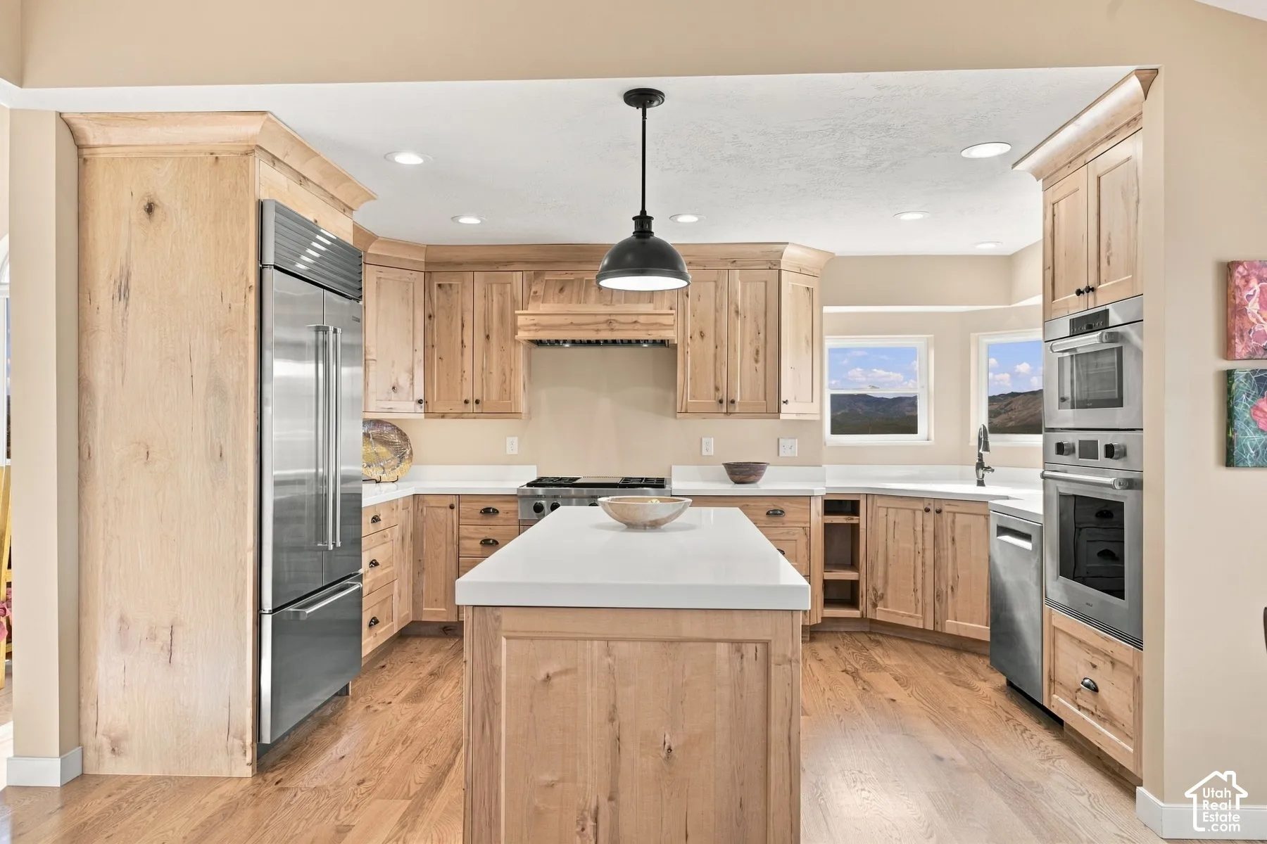 Kitchen featuring light wood cabinetry, white countertops, stainless steel appliances, a central island, and wood-finish flooring