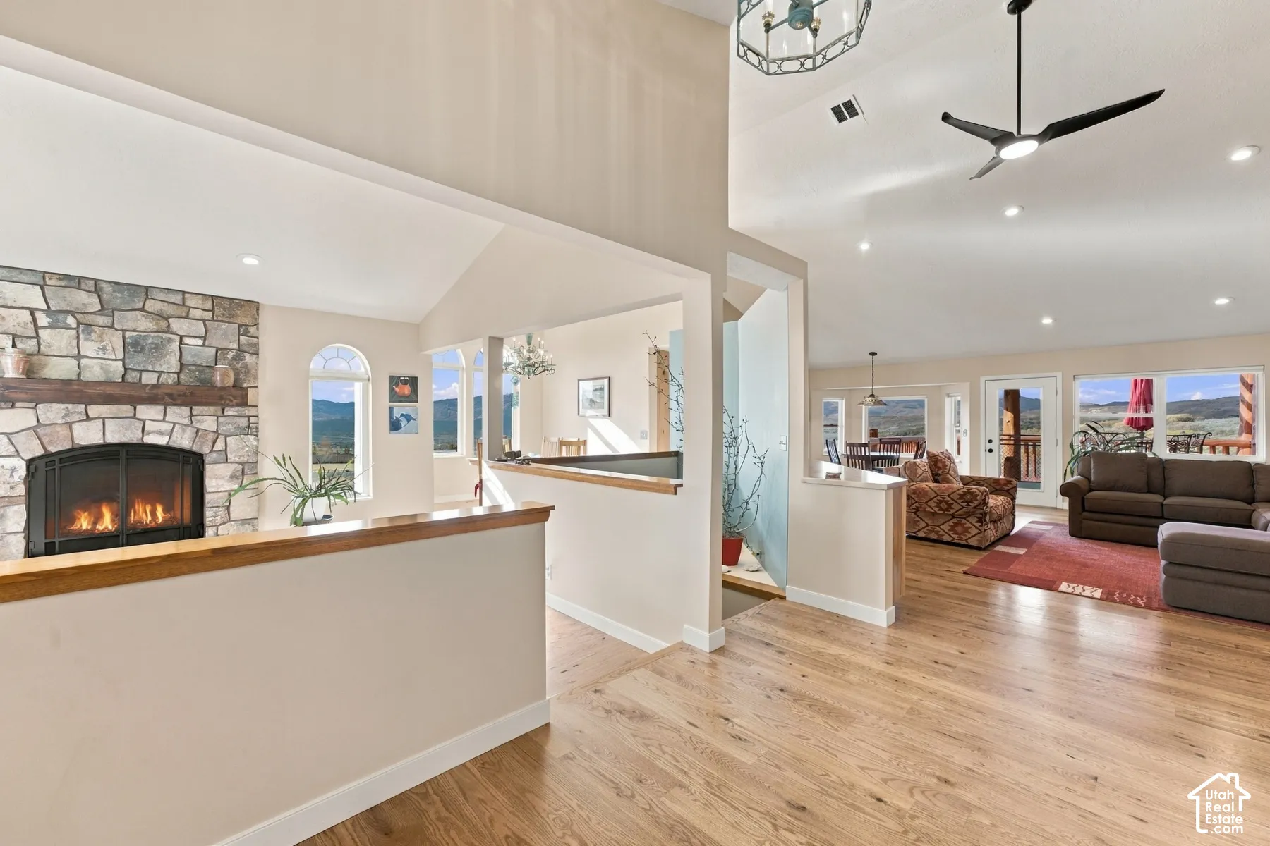 Vaulted ceilings, wood-finish flooring, floor-to-ceiling stone fireplace, arched windows, and recessed lighting