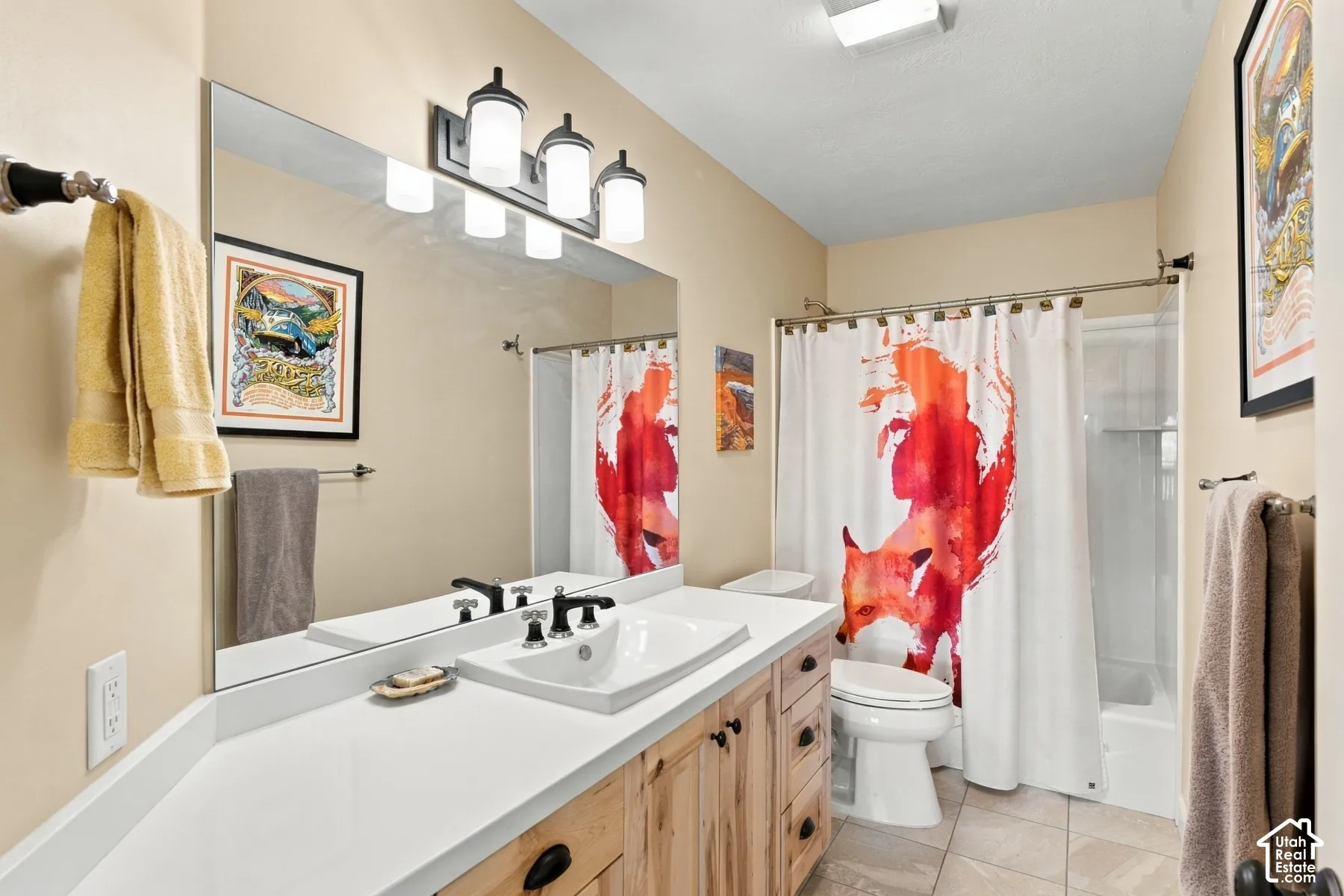 Bathroom featuring a custom wood-finish vanity, solid surface countertop with integrated sink, four-light vanity fixture, large wall-mounted mirror, and tile flooring