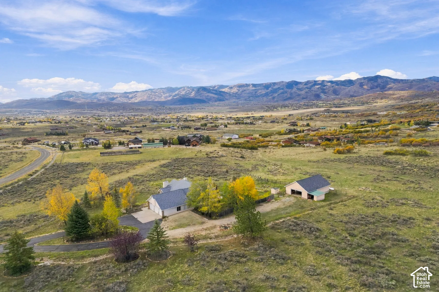 Aerial perspective of a multi-acre property featuring a single-story residence, a detached secondary structure, an asphalt driveway, and expansive mountainous terrain