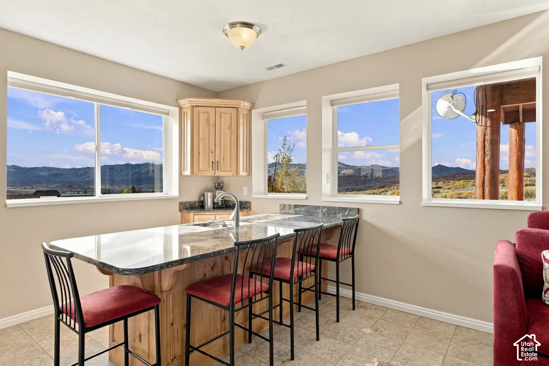 Kitchen island with stone-finish countertop, wood cabinetry, tile flooring, and multiple windows featuring mountain scenery