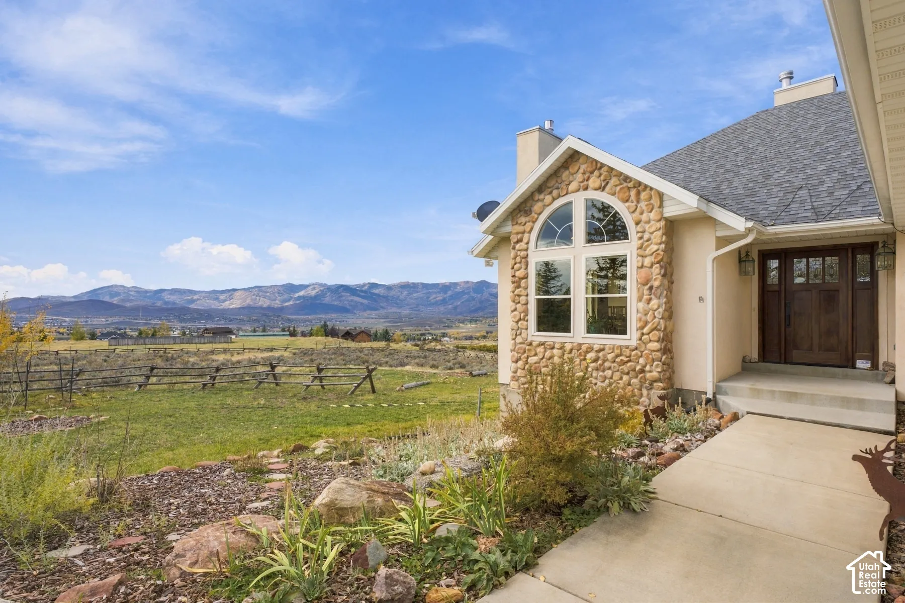 Exterior featuring natural stone masonry, an arched window, a wood-finish entry door, and a concrete walkway, set against a mountain backdrop