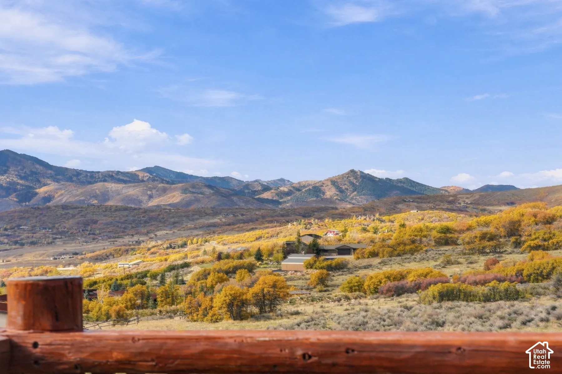 Polished timber log railing set against a backdrop of expansive mountain ranges and rolling terrain featuring deciduous trees