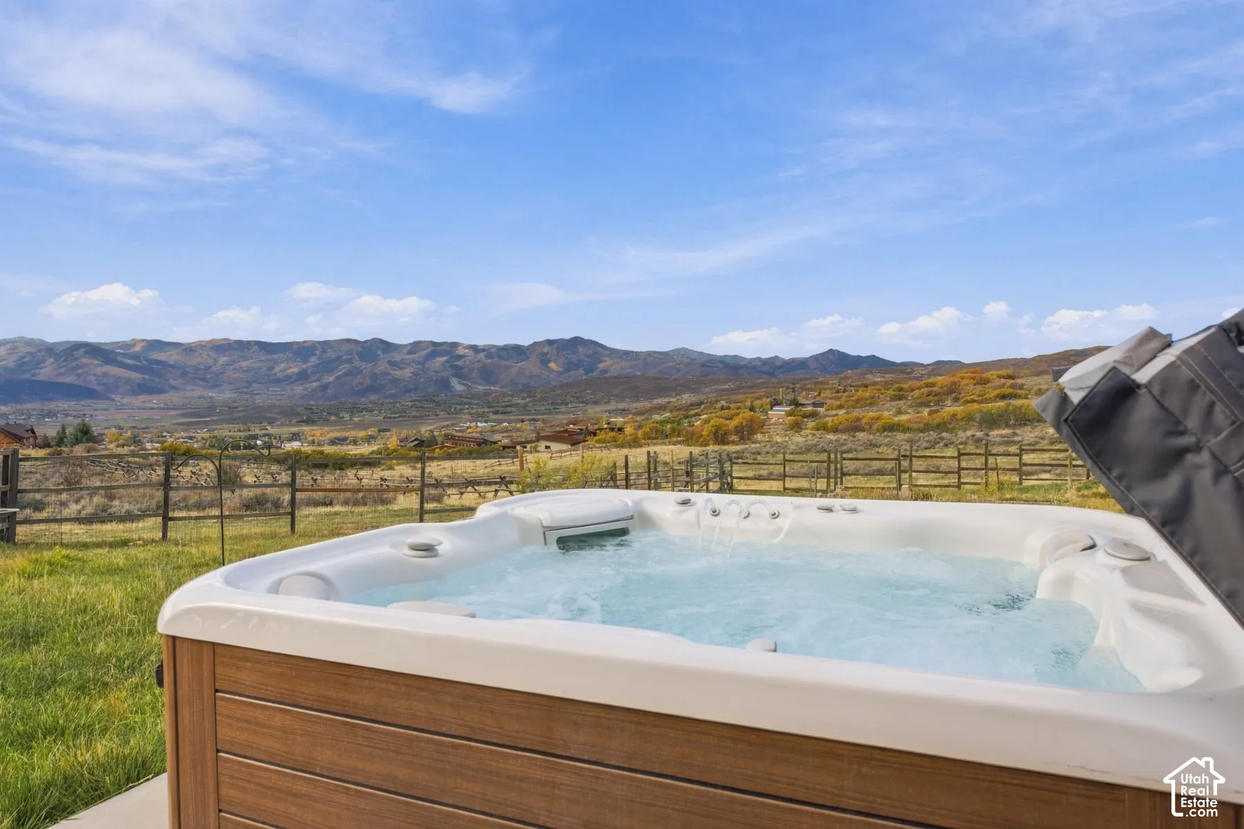 Built-in exterior jetted spa with wood-finish siding, situated on a lot featuring mountain scenery and post-and-rail fencing