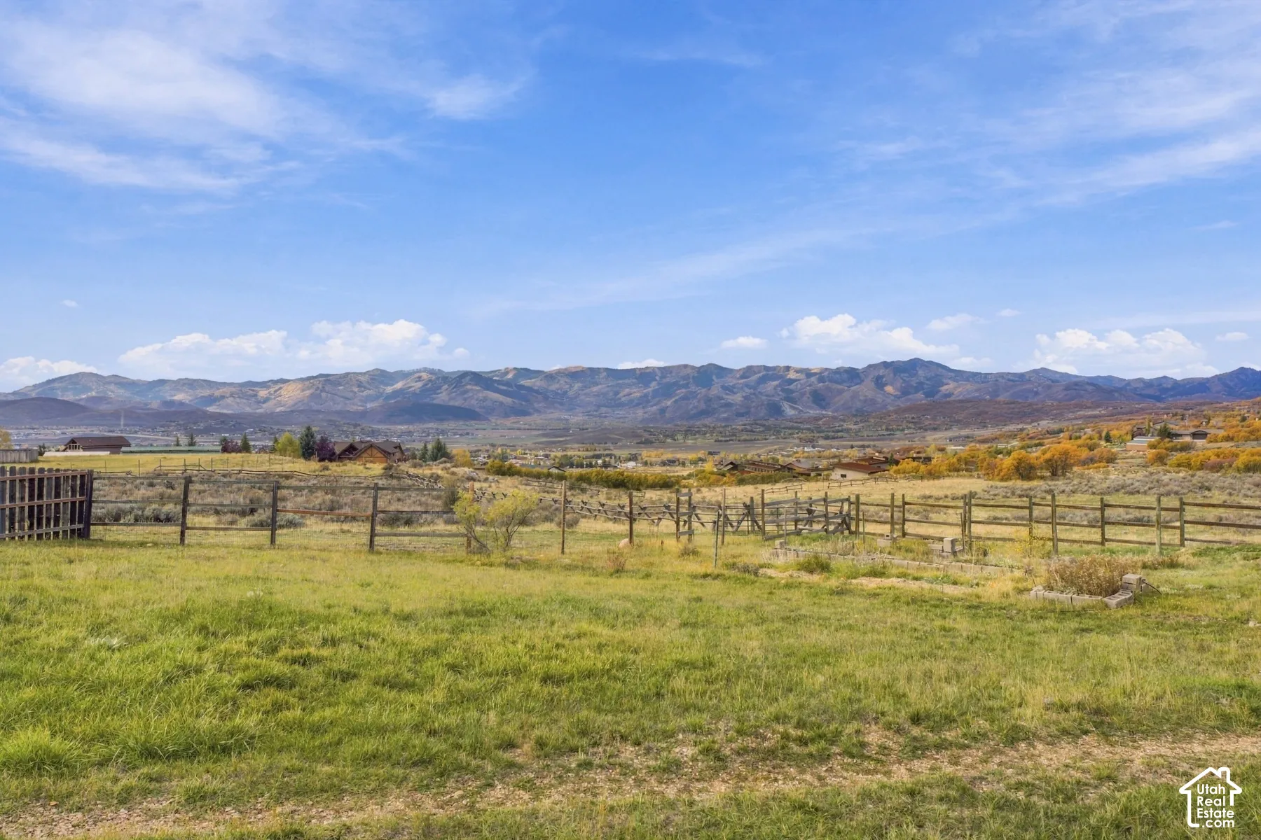 Expansive open lot featuring native grasses, wood post-and-rail fencing, and a mountain backdrop