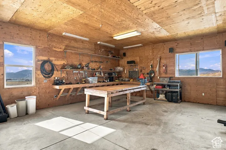 Workshop featuring wood-paneled walls, built-in wooden workbench, concrete flooring, fluorescent lighting, and dual windows