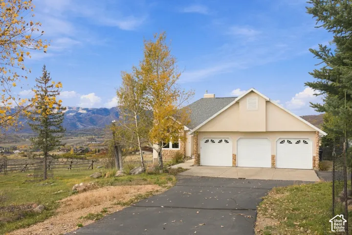 Single-story residence featuring a three-car garage, stone veneer accents, asphalt driveway, and mountain backdrop