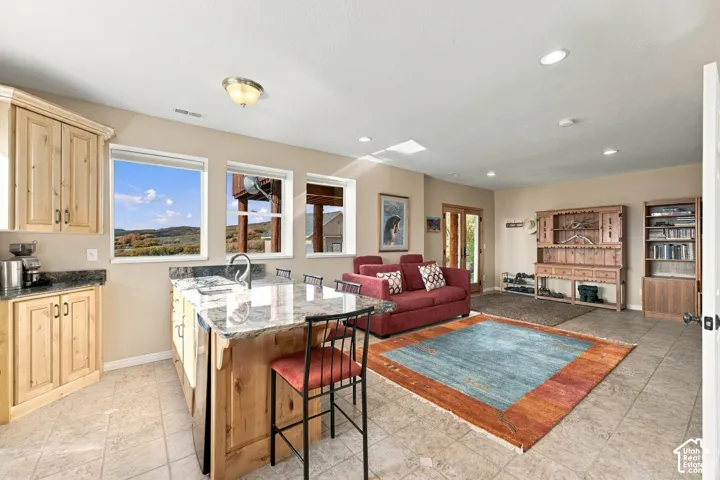 Kitchen featuring custom wood cabinetry, stone countertops, a central island, tile flooring, and recessed lighting