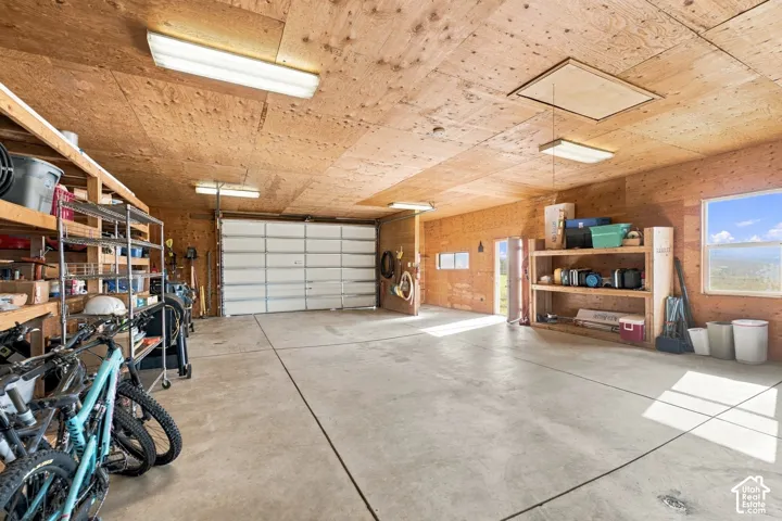 Multi-car garage featuring plywood-sheathed walls and ceiling, concrete flooring, overhead fluorescent lighting, and built-in wooden shelving units