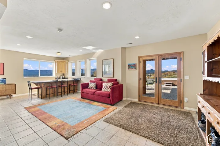 Open-concept living space featuring ceramic tile flooring, recessed lighting, a kitchen island with stone countertop, and double glass-paneled doors opening to an exterior patio