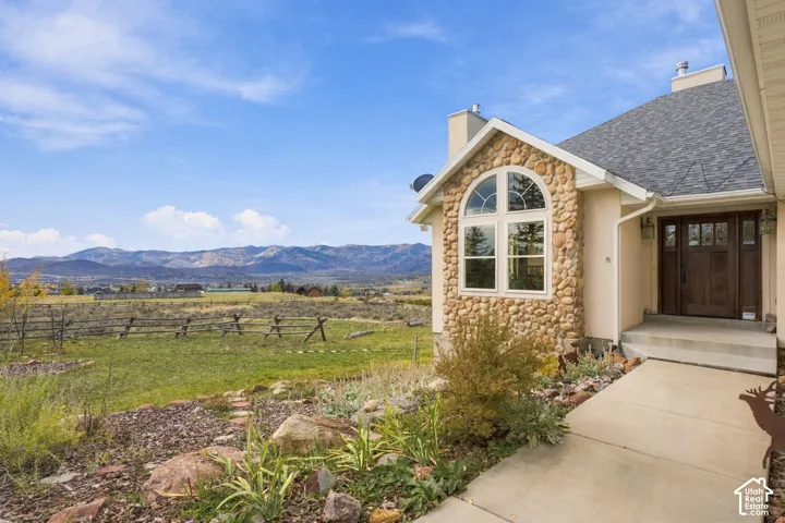 Exterior featuring natural stone masonry, an arched window, a wood-finish entry door, and a concrete walkway, set against a mountain backdrop