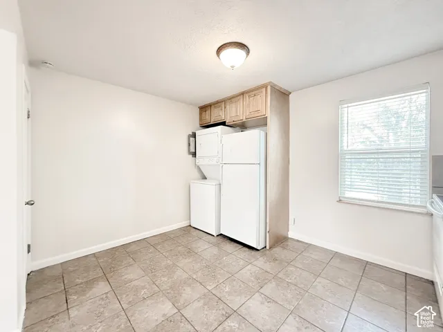 Neutral-toned tile flooring, overhead flush-mount lighting, custom wood-finish upper cabinetry, and a window featuring horizontal blinds